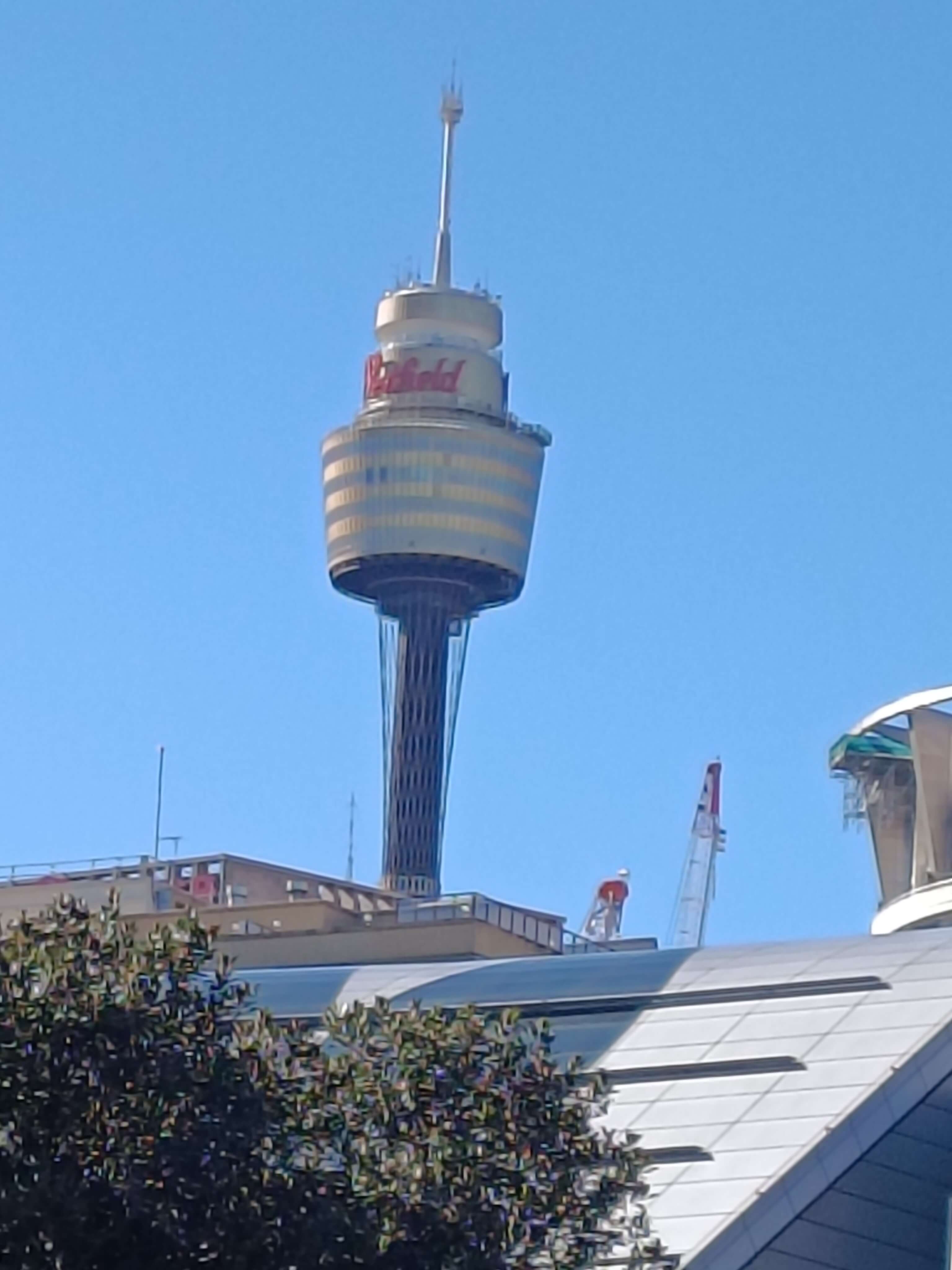A distant close-up of the Sydney Tower with a Westfield sign on it.